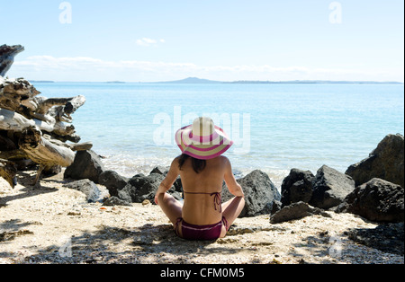 Une femme assise sur une belle plage de tranquillité portant un chapeau à large chapeau d'été. Banque D'Images