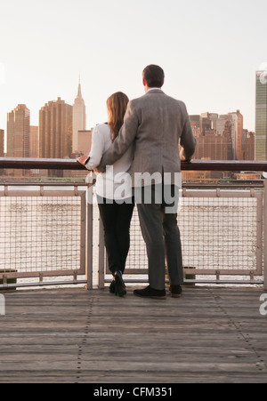 USA, New York, Long Island City, vue arrière du jeune couple standing on boardwalk, Manhattan skyline en arrière-plan Banque D'Images