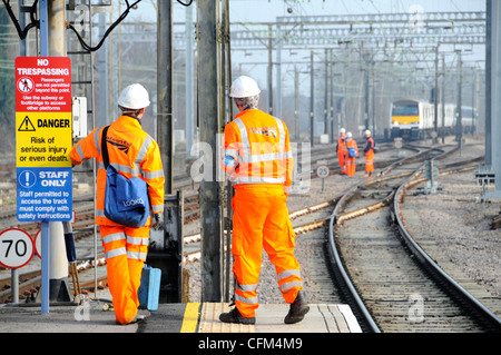 Network Rail Workmen vêtements de sécurité haute visibilité et casques de sécurité sur la plate-forme ferroviaire Groupe de travailleurs sur les voies au-delà du train distant Essex Angleterre Royaume-Uni Banque D'Images