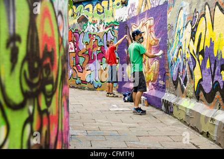 Vue horizontale vers le bas 'Allée Graffiti' sur Werregaran Straat à Gand, avec deux artistes pistolage leur art sur le mur. Banque D'Images