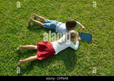 Children lying on grass, using digital tablet together Banque D'Images