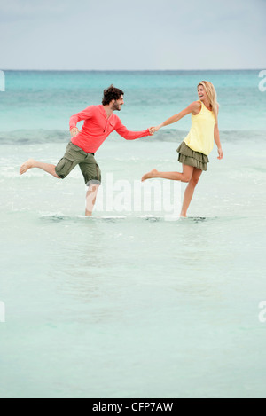 Couple debout sur une jambe dans l'eau à la plage, se tenant la main Banque D'Images
