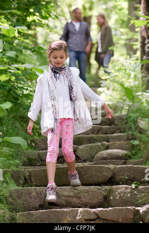 Fille qui marche vers le bas des marches en pierre dans les bois, les parents en arrière-plan Banque D'Images