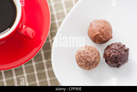Trois truffes au chocolat et une tasse de café rouge Banque D'Images