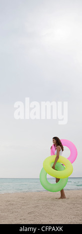 Woman standing on beach, holding inflatable rings, side view Banque D'Images