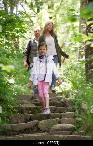 Fille qui marche vers le bas des marches en pierre dans les bois, les parents en arrière-plan Banque D'Images