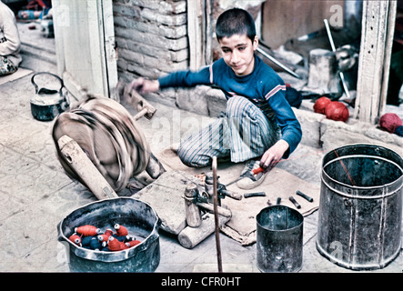 IRAN, Ispahan : Jeune garçon iranien à l'aide d'une manivelle en bois au vent sur un thread bobbin afin que son père puisse l'utiliser dans un métier Banque D'Images