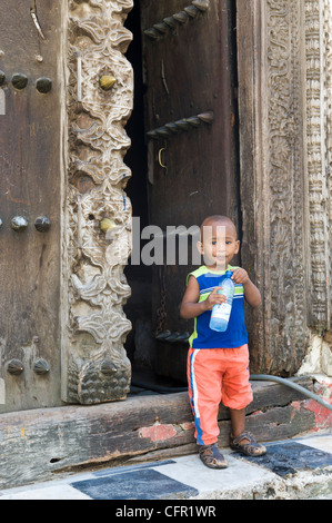 Garçon avec une bouteille d'eau debout à côté de la porte d'une vieille porte arabe à Stone Town Zanzibar Tanzanie Banque D'Images