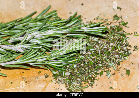 Branche de romarin frais haché herb (Rosmarinus officinalis) sur une planche à découper en bois. Banque D'Images