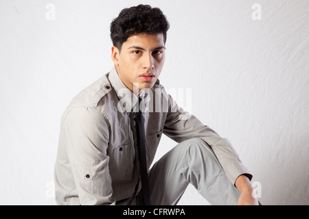 Beau jeune homme hispanique assise dans une chemise et cravate sombre, à la recherche d'une expression sérieuse et réfléchie à l'appareil photo Banque D'Images