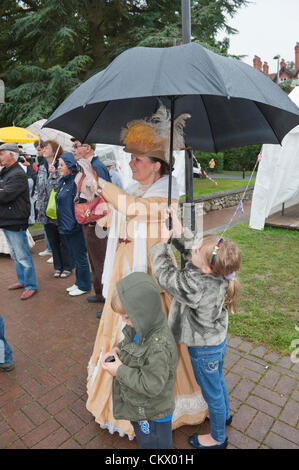 24 août, 2012. Llandrindod Wells, Pays de Galles, Royaume-Uni. Les enfants aident à protéger le costume d'une femme spectateur alors qu'elle prend une photo. En dépit de l'unseasonal,météo les participants sont dans la bonne humeur pour le 26ème Festival d'orgue qui est l'une des grandes attractions de l'époque victorienne semaine du Festival. Crédit photo : Graham M. Lawrence./Alamy Live News Banque D'Images