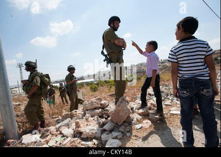 AL MASARA, CISJORDANIE - 31 août 2012 : un enfant palestinien défis un soldat israélien lourdement armés lors d'une manifestation hebdomadaire contre le mur de séparation. Banque D'Images