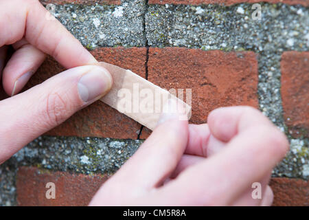 Les mains de l'homme d'appliquer du ruban adhésif sur les fissures de mur de briques. Plan horizontal. Banque D'Images