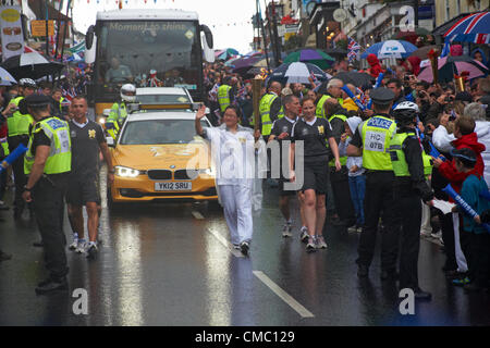 Lymington, Hampshire, Royaume-Uni samedi 14 juillet 2012. Relais de la flamme olympique à Lymington, Royaume-Uni. Le coureur Xingfen Wu porte le flambeau le long de Lymington High Street sous la pluie battante - relais de la torche olympique 2012, torche olympique 2012 Banque D'Images