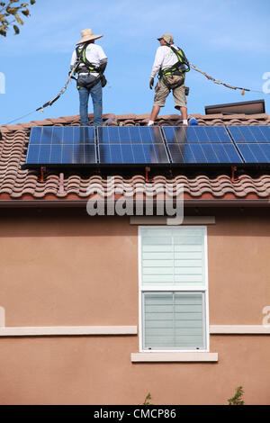 19 juillet 2012 - Aliso Viejo, Californie, États-Unis - les travailleurs de la construction d'installer des panneaux solaires sur une maison résidentielle toiture en Aliso Viejo, Californie. Location solaire pourrait être la section la plus forte croissance de l'énergie renouvelable le commerce comme 73  % des Californiens qui repose sur leur propriété PV solaire utilisent maintenant les entreprises de location. Des entreprises comme SunRun, Ville solaire, Sungevity, et l'énergie solaire la location de Californie sont entrés sur le marché de façon agressive. L'hypothèse que l'électricité du réseau les prix continueront d'augmenter à 7  %, un chiffre souvent cité par les sociétés de leasing, pourrait ne pas tenir dans le moyen terme. D Banque D'Images