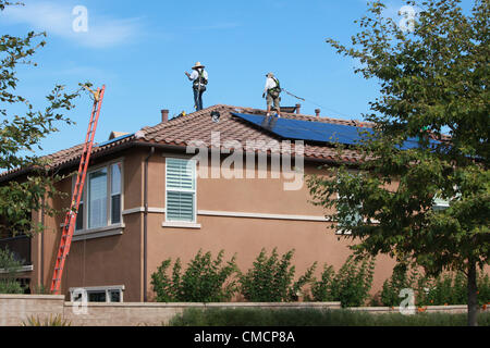 19 juillet 2012 - Aliso Viejo, Californie, États-Unis - les travailleurs de la construction d'installer des panneaux solaires sur une maison résidentielle toiture en Aliso Viejo, Californie. Location solaire pourrait être la section la plus forte croissance de l'énergie renouvelable le commerce comme 73  % des Californiens qui repose sur leur propriété PV maintenant utiliser l'énergie solaire les entreprises de location. Les entreprises d'énergie renouvelable comme SunRun, Ville solaire, Sungevity, et l'énergie solaire la location de Californie sont entrés sur le marché de façon agressive. L'hypothèse que l'électricité du réseau les prix continueront d'augmenter à 7  %, un chiffre souvent cité par les sociétés de leasing, pourrait ne pas tenir Banque D'Images