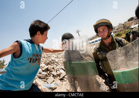 AL MASARA, TERRITOIRES PALESTINIENS - le 20 juillet 2012 : un garçon palestinien pousse contre le bouclier anti-émeute lourdement armés d'un soldat israélien dans une non-violente hebdomadaire manifestation contre le mur de séparation israélien en Cisjordanie, Al-Masara, le 20 juillet 2012. Si le tracé de la barrière de séparation est réalisé comme prévu, il coupera le village de Al-Masara provenant des terres agricoles appartenant aux habitants du village. Banque D'Images