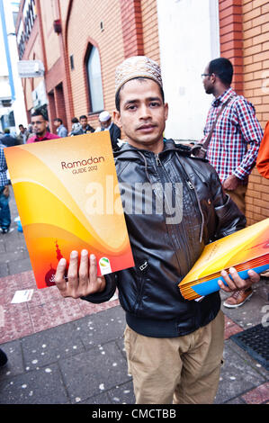 Londres, Royaume-Uni - 20 juillet 2012 : un homme distribue le Ramadan 2012 Guide à l'extérieur de la mosquée est de Londres, le plus important de Grande-Bretagne, juste après la célébration de la prière du vendredi, le premier jour du Ramadan. Banque D'Images