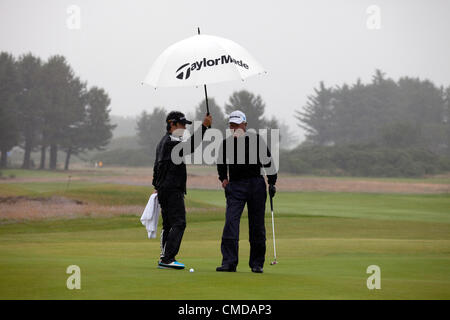 23 juillet 2012, Kilmarnock (Barassie) Golf Club, Troon, Ayrshire, Scotland, UK, Isao Aoki, depuis le Japon, golfeur professionnel, sur le 18ème green à l'abri de la pluie avec son caddy tenant un parapluie. Il est en compétition dans la Royal and Ancient ouvert Senior compétition de qualification, 2012. Banque D'Images