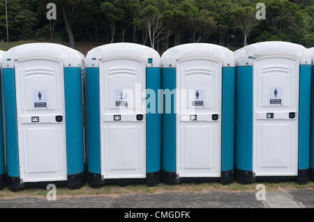 Rangée de toilettes portables bleues et blanches alignées dans un espace extérieur avec forêt en arrière-plan. Banque D'Images