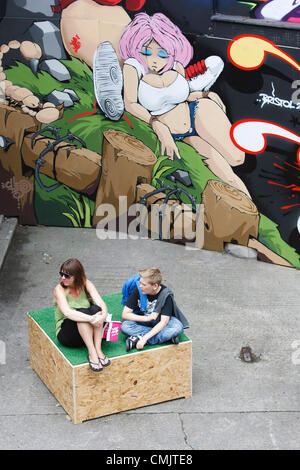 Bristol, Royaume-Uni. 18 août 2012. Une femme et un enfant sont photographiés assis devant l'une des œuvres d'art qui ont été peintes sur des bâtiments de Nelson Street pour le festival d'art de rue See No Evil. See No Evil est une collection d'œuvres d'art public créées par de multiples graffitis et artistes de rue urbains situés dans et autour de Nelson Street à Bristol, au Royaume-Uni. Banque D'Images