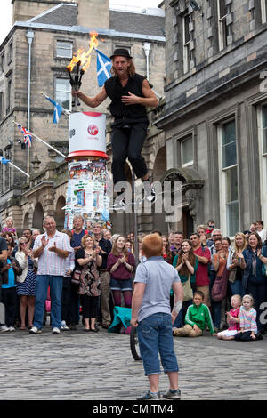 18 août 2012 Damien Ryan, un artiste de rue, école d'un monocycle et jonglerie avec torches de feu dans le Royal Mile, au cours de l'Edinburgh Fringe Festival. Un petit garçon qui avait été l'aider pendant son spectacle, les regarde. Banque D'Images