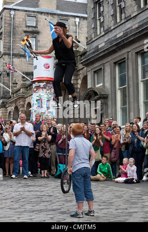 18 août 2012 Damien Ryan, un artiste de rue, école d'un monocycle et jonglerie avec torches de feu dans le Royal Mile, au cours de l'Edinburgh Fringe Festival. Un petit garçon qui avait été l'aider pendant son spectacle, les regarde. Banque D'Images