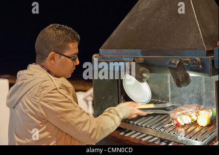 Chef de la cuisson des aliments sur le front de mer de Benalmadena à l'extérieur sur un barbecue au charbon de bois chaud Banque D'Images