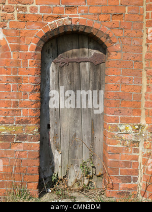 Une vieille porte en bois en décomposition dans une porte voûtée dans un très vieux mur en briques rouges. Banque D'Images