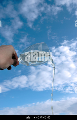 Un verre d'eau est versé sur un fond de ciel bleu nuageux lumineux Banque D'Images