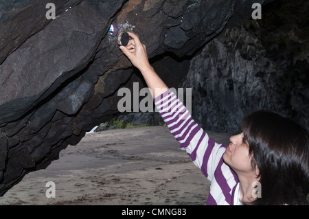 Conteneur de chasse au trésor / affichage du contenu - personne récupérant un conteneur de chasse au trésor caché dans une crevasse de roche lors d'une aventure de chasse au trésor en plein air. Banque D'Images