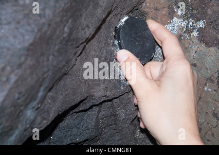 Conteneur de chasse au trésor / affichage du contenu - personne récupérant un conteneur de chasse au trésor caché dans une crevasse de roche lors d'une aventure de chasse au trésor en plein air. Banque D'Images