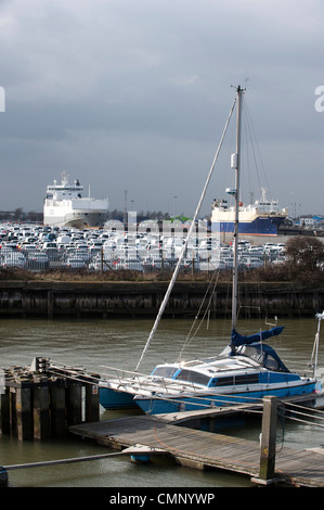 Voitures garées à Grimsby Docks qui ont été importées et exportées par les navires dans l'arrière-plan. Un yacht dans la marina. Banque D'Images