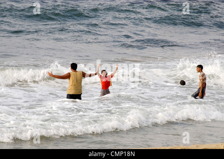 Apollonia. La Libye. Les garçons libyen vêtu et brandissant une éclaboussure dans les eaux de la Jamahiriya / Méditerranée sur la plage de sable Banque D'Images