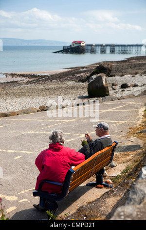 Royaume-uni, Pays de Galles, Swansea, Mumbles, couple assis sur un banc de pique-nique de manger au soleil donnant sur la Baie de Swansea Banque D'Images