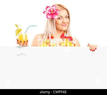 Jolie femme vêtue d'un costume hawaïen holding a cocktail et posant derrière un panneau blanc Banque D'Images