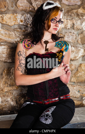 Une femme brune vêtue de vêtements steampunk themed pose avec des lunettes sur la tête. Banque D'Images