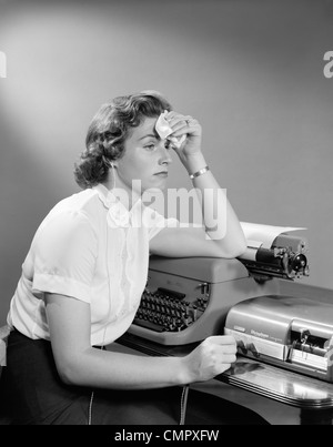 1950 FEMME MALADE SITTING AT DESK SECRÉTAIRE AVEC MACHINE À ÉCRIRE ET LA DICTÉE MACHINE PROPOSANT MOUCHOIR À FRONT Banque D'Images