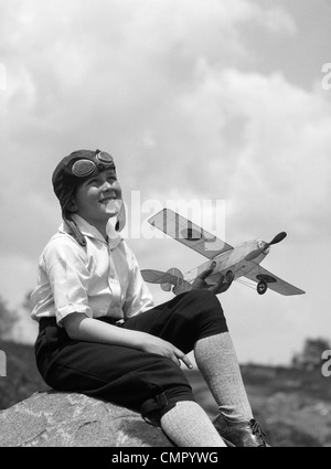 1930 garçon EN CUIR AVIATOR CAP AVEC LUNETTES ASSIS SUR LA ROCHE HOLDING MODEL PLANE Banque D'Images