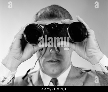 1960 HEAD-ON CLOSE-UP OF MAN LOOKING THROUGH BINOCULARS Banque D'Images