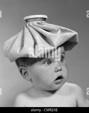 1960 BÉBÉ PORTRAIT les yeux écarquillés avec bouche ouverte et PAQUET DE GLACE SUR LA TÊTE À LA RECHERCHE DE CÔTÉ Banque D'Images