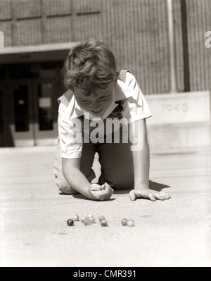 1950 SMILING BOY PRÊT À TIRER à genoux SUR LA COUR DE L'ÉCOLE JOUER JEU DE BILLES Banque D'Images