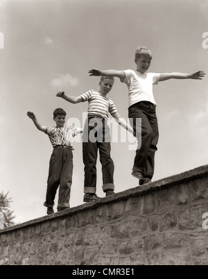 1950 Trois garçons RIRE MARCHER SUR LE DESSUS DE MUR DE PIERRE LES BRAS À L'ÉQUILIBRAGE DE SUIVRE LE CHEF Banque D'Images