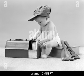 1940 BÉBÉ EN INGÉNIEUR FERROVIAIRE HAT TIRANT BOUTEILLE DE LAIT À PARTIR DE LA BOÎTE À LUNCH AVEC HAMMER & OUTILS CLÉ À SIDE STUDIO Banque D'Images