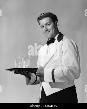 1950 SMILING WAITER BOW TIE & veste blanche avec garniture noire COLLIER CHESTERFIELD HOLDING PLATEAU LOOKING AT CAMERA Banque D'Images