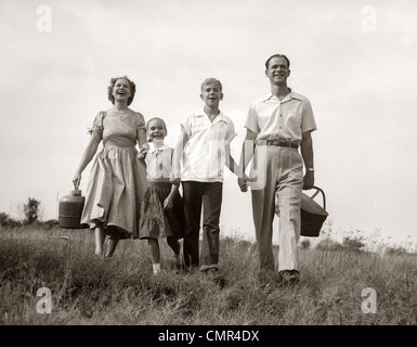 1950 FAMILY WALKING IN GRASSY MEADOW exerçant son panier de pique-nique de l'été et le Thermos Banque D'Images