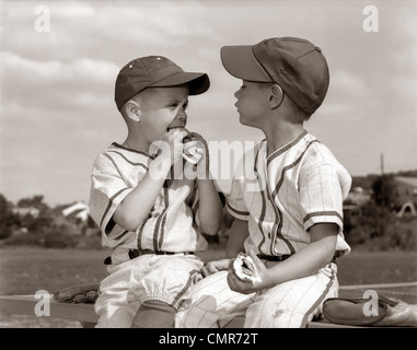 1960 LA PETITE LIGUE DE BASEBALL BOYS EN MAJUSCULES ET LES UNIFORMES de manger des hot dogs Banque D'Images