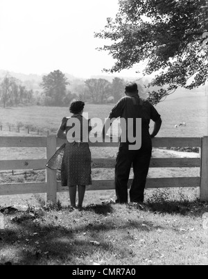 1940 VUE ARRIÈRE DE LA FERME ÂGÉS COUPLE STANDING AT FENCE sur pâturage Banque D'Images