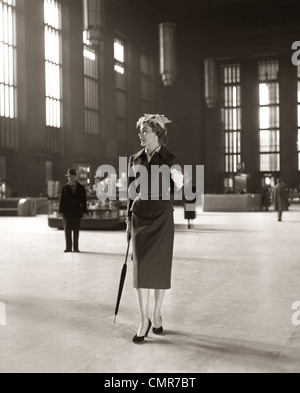 1950 HAUT DE GAMME À LA MODE FEMME SEULE GARE D'ATTENTE PARAPLUIE LONELY Banque D'Images