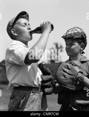 1930 PAIRE DE GARÇONS EN UN AVEC DES GANTS DE BASEBALL CATCHER s'observer d'autres MASQUE WEARING CAP VERRE BOUTEILLE DE SODA Banque D'Images